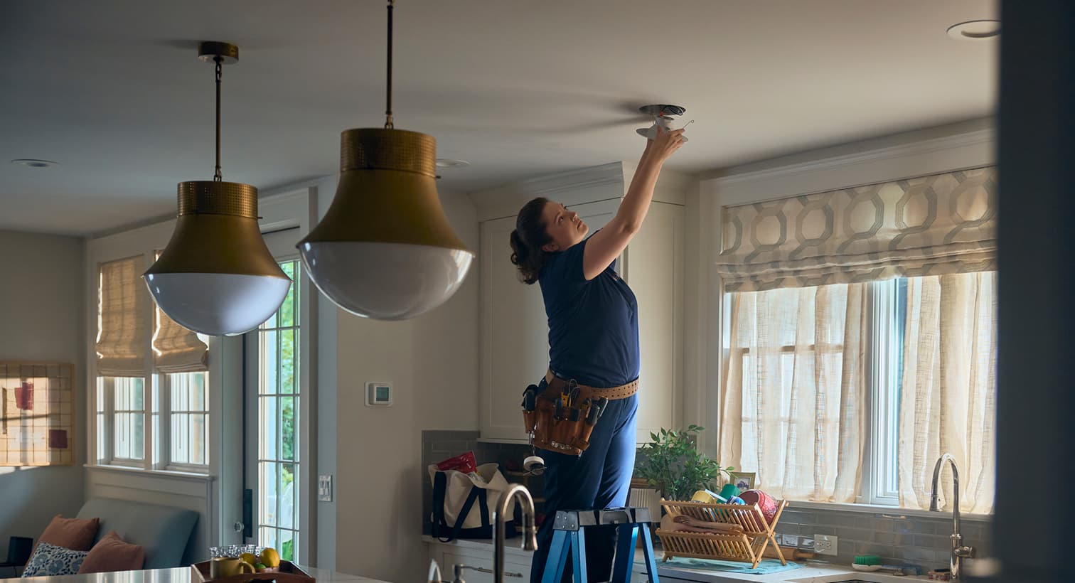 A professional Performance electrician standing on a ladder to install modern recessed ceiling lights during a residential electrical installation service.