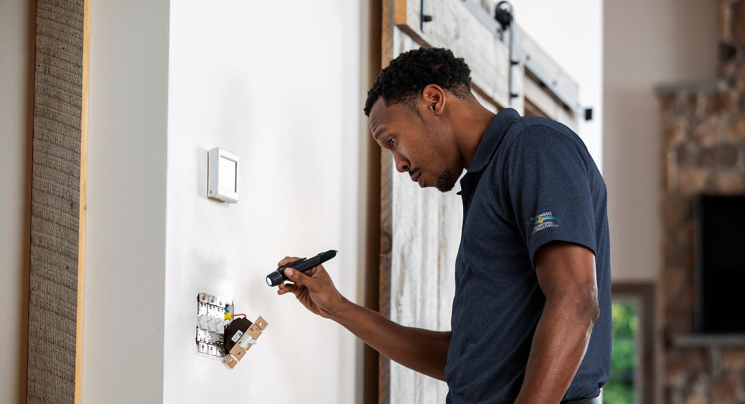 A professional Performance electrician using a flashlight to safely inspect and troubleshoot exposed residential wall switch wiring during an electrical repair service.