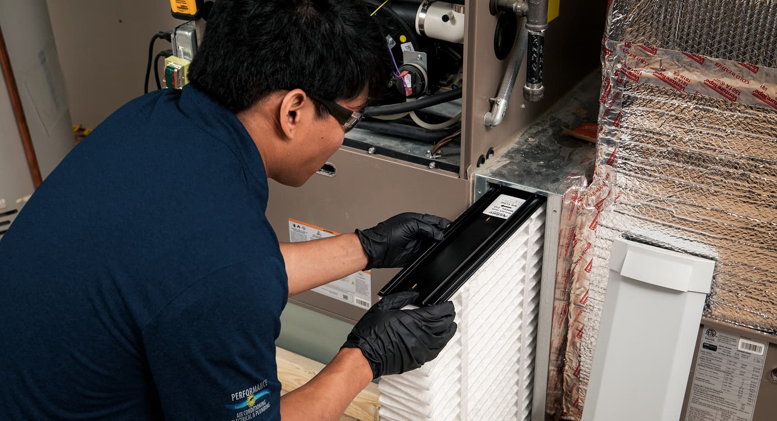 A professional Performance HVAC technician replacing a clean pleated air filter in an indoor air handler unit during a routine AC maintenance tune-up.